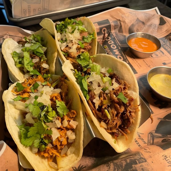 Four Cuban tacos with shredded meat, cilantro, and diced onions, served with two dipping sauces.