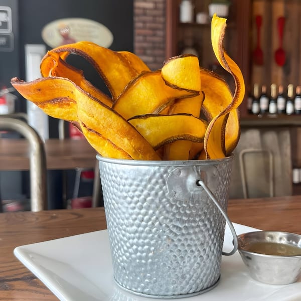 Crispy, golden-brown plantain chips served in a hammered metal bucket with a side of dipping sauce.