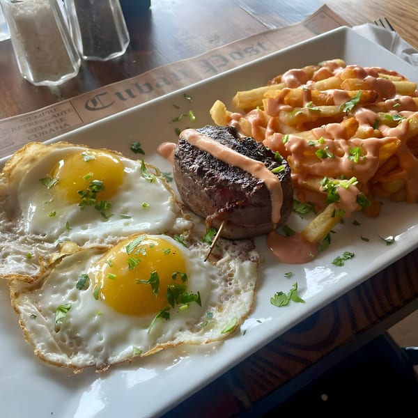Cuban steak and eggs with fries, drizzled with pink sauce and garnished with parsley.